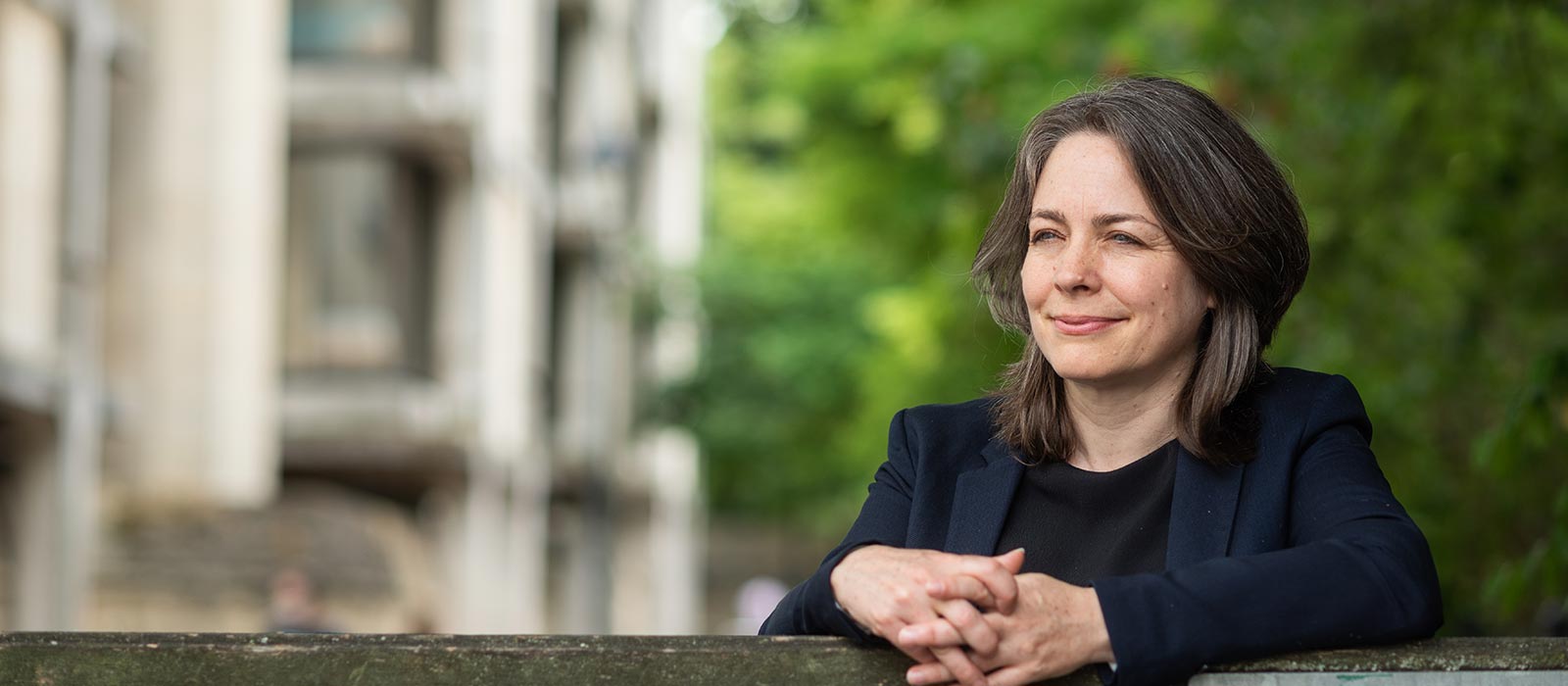 Professor Cathy Cresswell leaning against a bright red brick wall in central Oxford